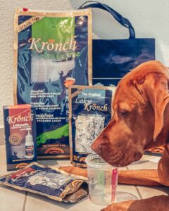 Magya liegt vor dem großen Futterpaket von Henne Pet Food