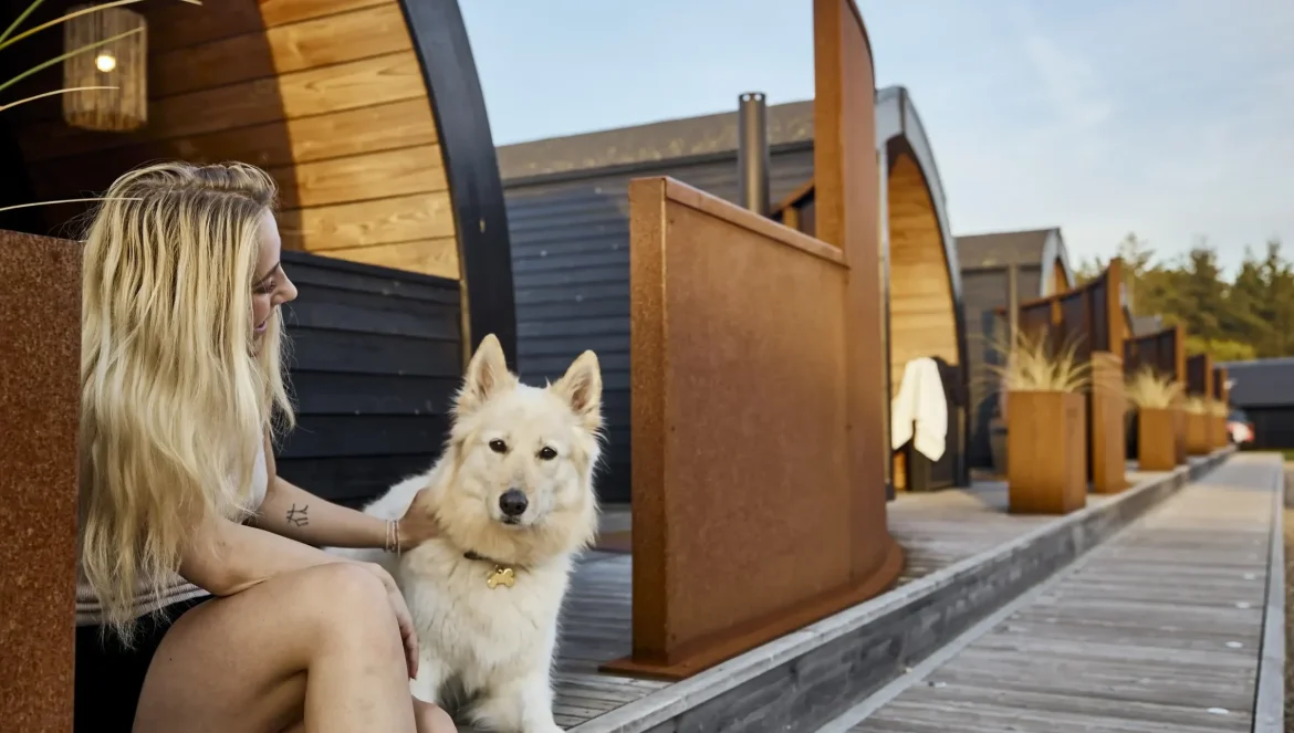 Henne Strand Resort - Frau sitzt mit ihrem Hund auf einer Stufe vor ihrem Ferienhaus