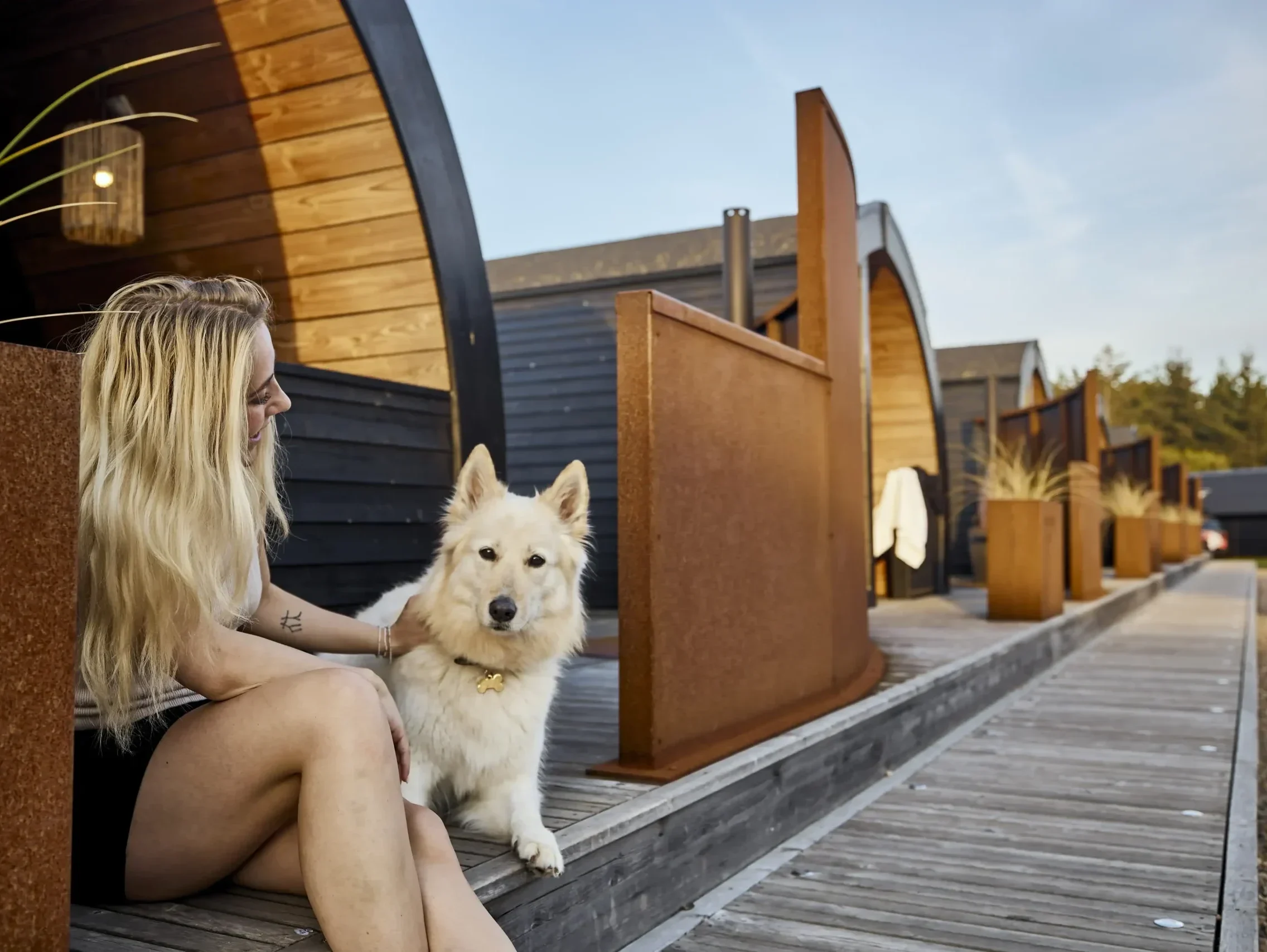 Henne Strand Resort - Frau sitzt mit ihrem Hund auf einer Stufe vor ihrem Ferienhaus