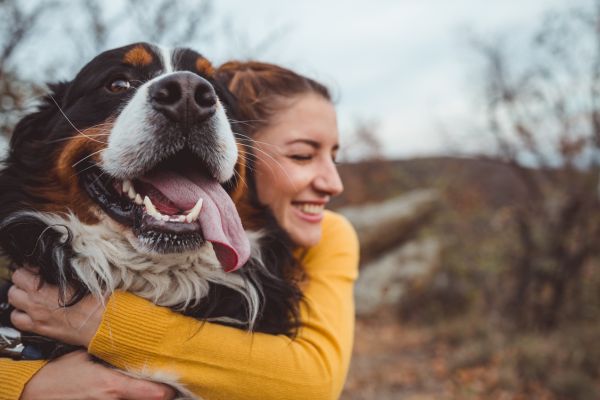 Frau lacht und umarmt ihren Hund. Dieser schaut auch freudig. 