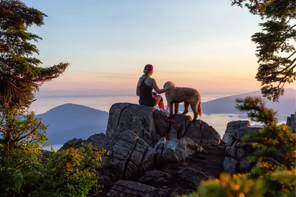 Herchen und Hund sitzen nebeneinander auf einem Fels und schauen in den Sonnenuntergang