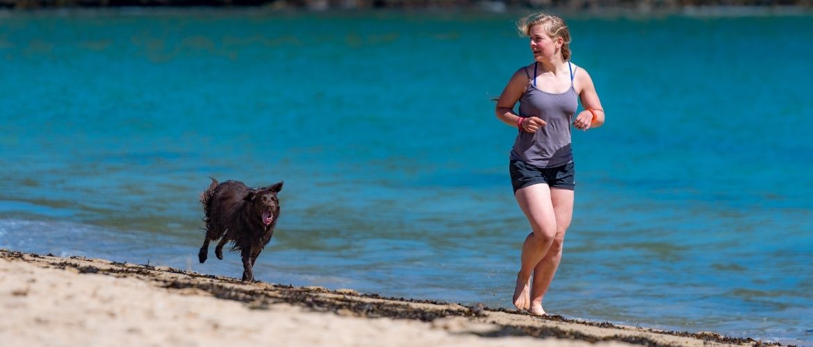 Frau joggt mit Hund am Strand